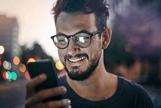 Person holding and looking at a smartphone outdoors at night; background lights and face are blurred.