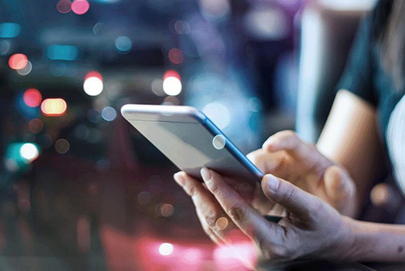 Close-up of hands using a smartphone with blurred colorful city lights in the background.