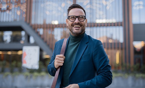 Person in blue blazer and green turtleneck standing in front of a modern building with wooden slats.