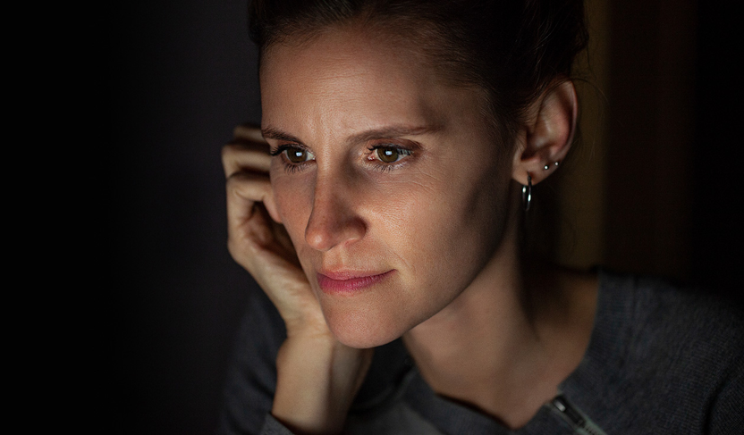 Person sitting in dim lighting with visible ear piercings and a relaxed pose.