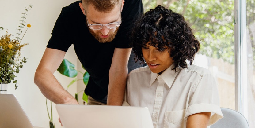 Two colleagues working together at a laptop in a bright, modern workspace.