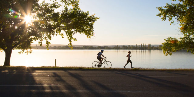Cyclist and runner enjoying outdoor exercise along a lakeside path at sunrise.
