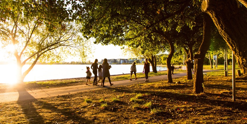 Group of people walking along a scenic lakeside path at sunset.