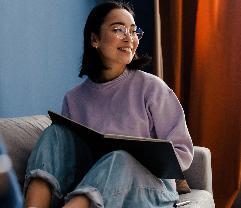 A person sits on a couch holding an open book in a relaxed indoor setting.